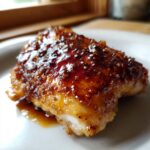 Close-up of a juicy piece of honey garlic chicken coated in a thick, caramelized, glossy sauce.
