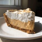 A thick slice of no bake peanut butter pie featuring a graham cracker crust, creamy peanut butter filling, and fluffy white topping.
