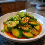Close-up of a vibrant asian cucumber salad, featuring sliced cucumbers in chili oil, topped with sesame seeds and green onions.