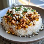 A close-up of a street corn chicken rice bowl featuring white rice topped with seasoned chicken, corn, cotija cheese, and cilantro.